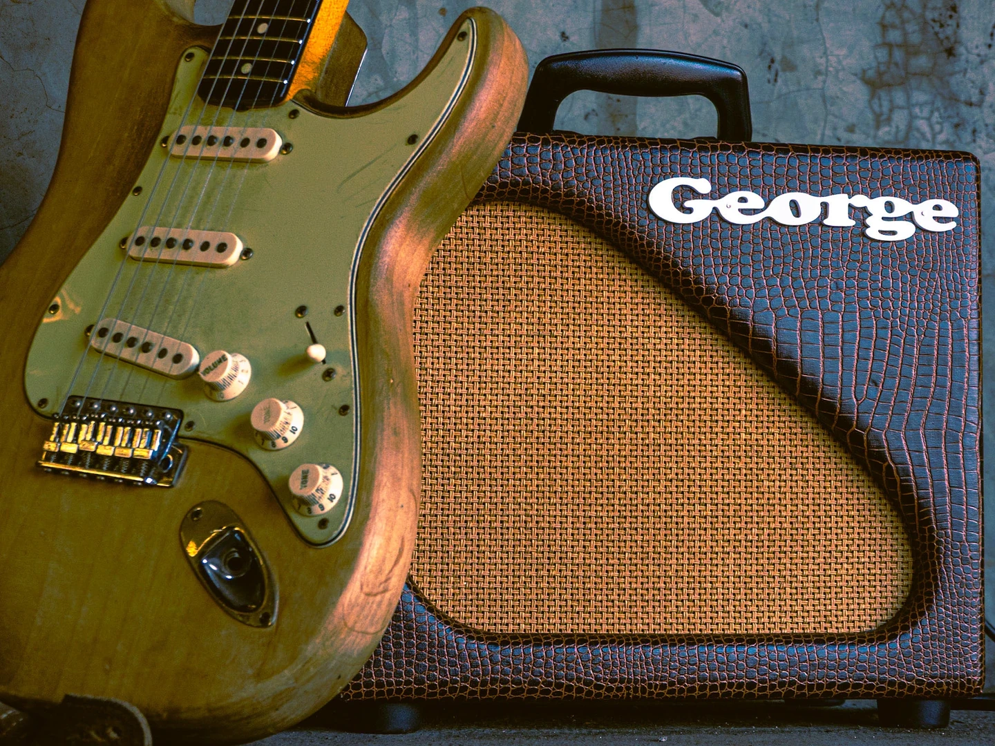 Detalle del logo George en el amplificador junto a una guitarra Stratocaster